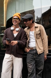 A joyful gay couple shares a moment of laughter while looking at a smartphone. They stand together