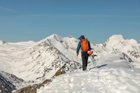 Back view of an unrecognizable person hiking up a snow-covered mountain with a snowboard. The