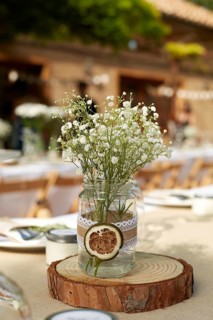 A rustic wedding table centerpiece featuring delicate white flowers in a mason jar adorned with