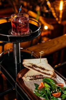 A gourmet club sandwich filled with tender veal cheeks, served alongside a fresh tomato and spinach
