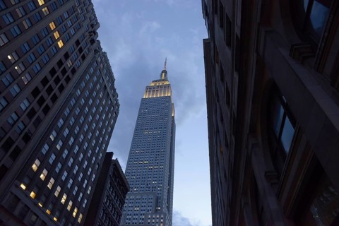 Low angle of the Empire State Building towers majestically between neighboring skyscrapers in