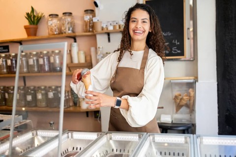 A cheerful woman working in an ice cream shop, serving a scoop of delicious ice cream in a cone.