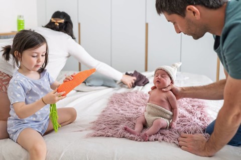 A young family shares tender moments with their newborn baby and big sister. The joyful scene