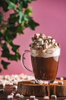 Hot chocolate with whipped cream, cocoa powder and marshmallows on a wooden board, pink background