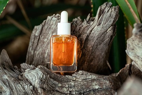 A clear bottle of Vitamin C serum for face care is displayed in a rustic wooden setting surrounded