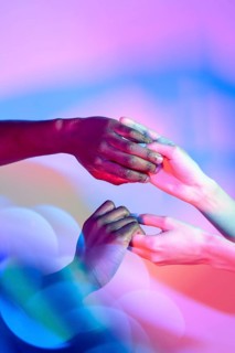Multiethnic hands gently holding each other with vibrant colored lighting in the background,
