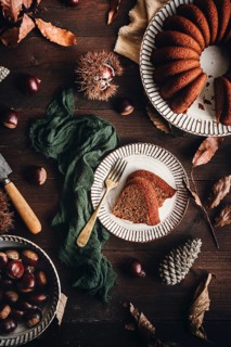 A beautifully styled chestnut cake on a ceramic plate, surrounded by whole chestnuts, leaves, and