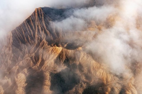 Aerial view of rugged mountain peaks partially covered by mist, creating a dramatic and serene