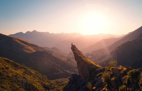 A breathtaking view of a hiker standing on a mountain peak, bathed in the golden light of a sunrise