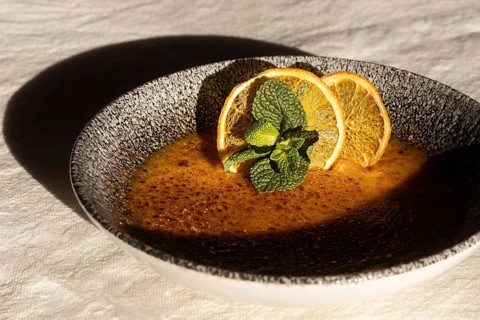 A caramel dessert elegantly served in a dark textured bowl, topped with dried orange slices and