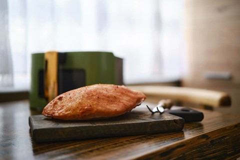 Roasted pork fillet rests on a wooden cutting board in a kitchen table. Air fryer basket and