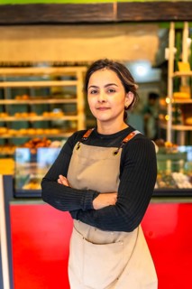Vertical photo of a latin confident woman worker wearing apron standing proud in a bakery shop