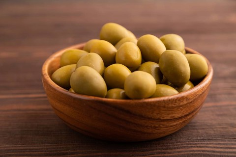 Fresh green olives in wooden bowl on brown wooden background. side view, close up, selective focus