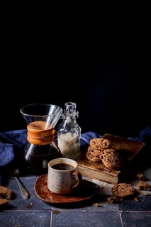 A cozy setup featuring a rustic ceramic cup of coffee, a glass bottle of milk, and a stack of