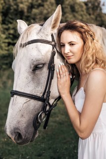 A young woman in a white dress gently embraces a serene white horse outdoors, showcasing a peaceful