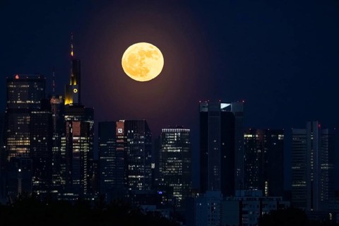 The full moon passes behind the Frankfurt banking skyline, Frankfurt am Main, Hesse, Germany
