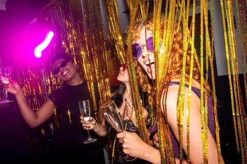 Young women enjoying a vibrant disco party, holding sparkling wine glasses and posing behind