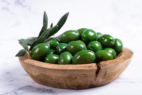 Halkidiki olives, classic Greek green olives, in a wooden bowl, on a marble table, no people