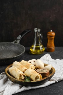 Freshly prepared vegetarian crepes with mushrooms on a wooden plate. A frying pan and olive oil