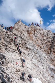 Tourists queue up for the summit of the Zugspitze, summit with golden summit cross, overtourism,