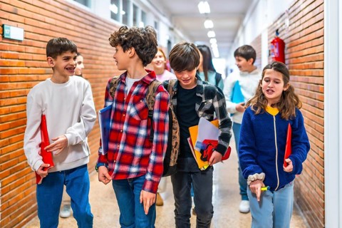 Cheerful pupils carrying books and chatting together while walking down school corridor between