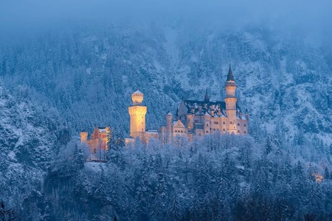 The illuminated castle appears mystical in a snow-covered landscape at night, Neuschwanstein,