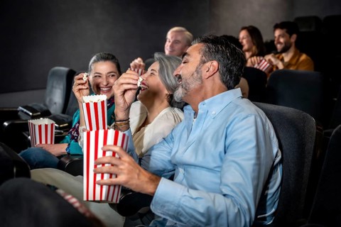 Groups of friends laughing and enjoying popcorn while watching an exciting movie in a cozy cinema