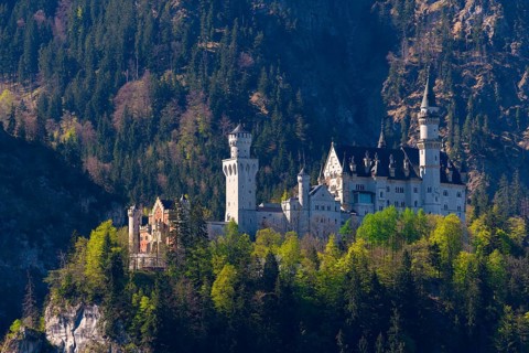 A majestic castle towers high above wooded cliffs, surrounded by unspoilt nature and mountains,