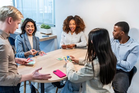 Multi ethnic businesspeople enjoying a lively card game break, laughing and bonding in a modern