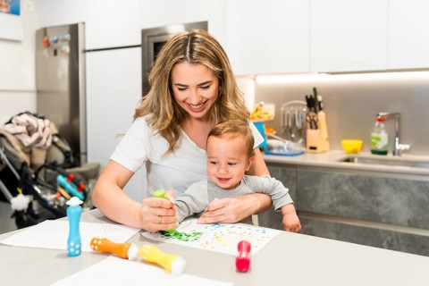 Happy mother and baby boy enjoying creative playtime, painting with colorful dot markers at the