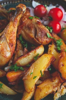 Fried chicken legs with potato slices, on a plate, baked in the oven, with spices, homemade, no