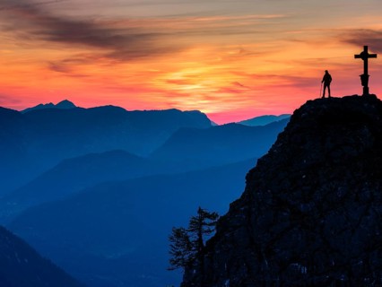 Mountaineer at the summit cross of the Kleiner Jenner at dusk, Reiteralpe in the background,