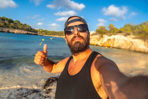 Bearded man with sunglasses and baseball cap taking selfie on beautiful s'amarador beach, mallorca,