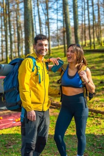 Hikers smiling and enjoying their camping adventure in the serene woods, surrounded by lush trees