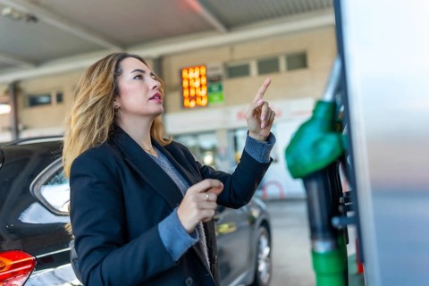 Woman at a gas station pointing at the illuminated price sign, contemplating rising fuel costs