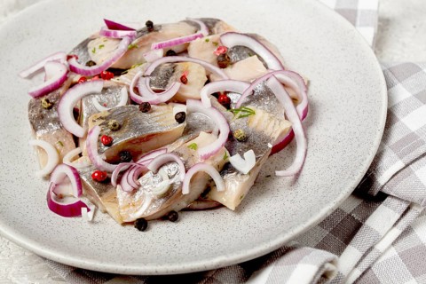 Salted herring, with spices and red onion, sliced fillet, on a plate, top view