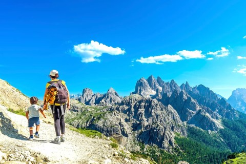 Mother and son walking on a mountain trail in the dolomites, enjoying the breathtaking view of the