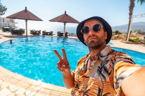 Tourist man in the hotel pool in summer taking a selfie enjoying the vacation