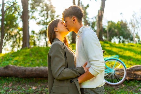 Romantic couple kissing in a park during golden hour, with their bicycle resting nearby,