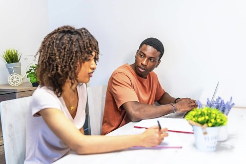 Young man and woman using laptop and taking notes while working from home, managing domestic