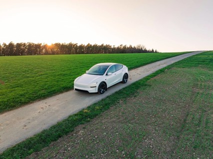 An electric vehicle drives along a remote country road, with sweeping views over fields and a