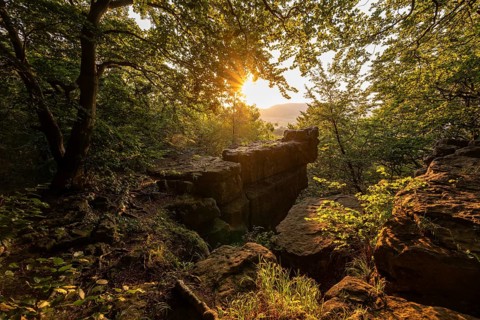 A dramatic sunset bathing a mighty rock spur and trees in the forest in golden light, Kanstein,