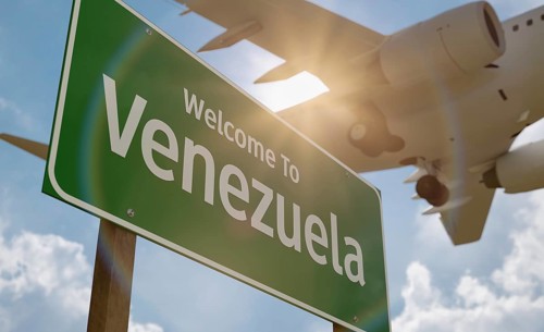 Welcome to Venezuela green road sign with low flying airplane just above with landing gear down