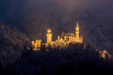 A castle stretches majestically in the darkness, illuminated against a snow-covered slope,