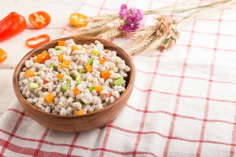 Pearl barley porridge with vegetables in wooden bowl on a white wooden background and linen textile