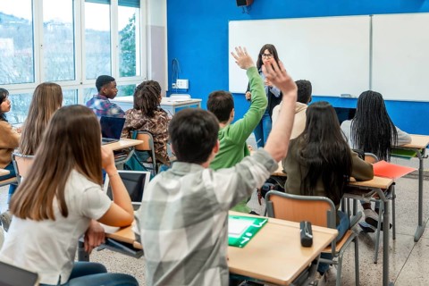 Diverse group of teenage high school students raising hands to answer teacher's question during
