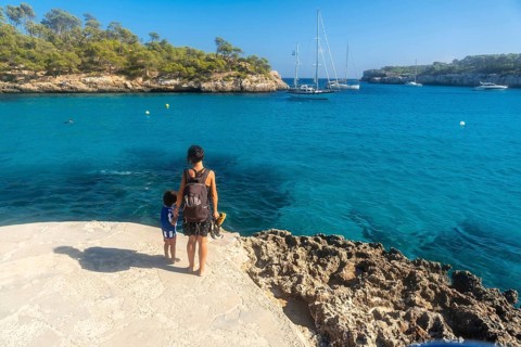Mother and son standing on a cliff, enjoying breathtaking view of sailboats anchored in the