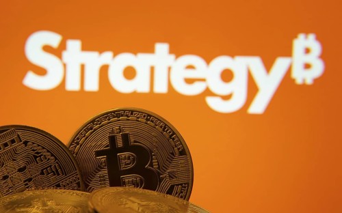 Close-up of Bitcoin coins with the MicroStrategy logo visible on a screen in the background