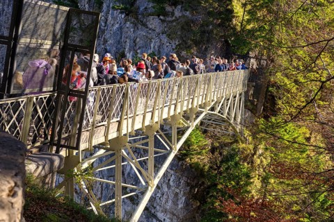 People standing on the Marienbrücke in a forest area surrounded by mountains, autumn atmosphere and