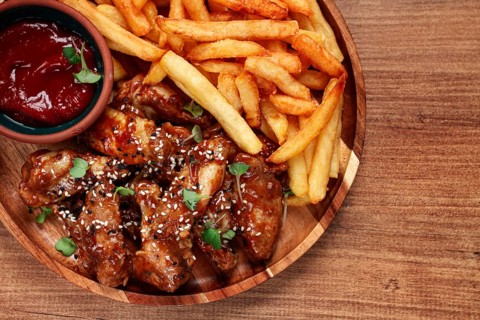 Barbecue chicken wings, sprinkled with sesame seeds, with French fries, and sauce, on a wooden